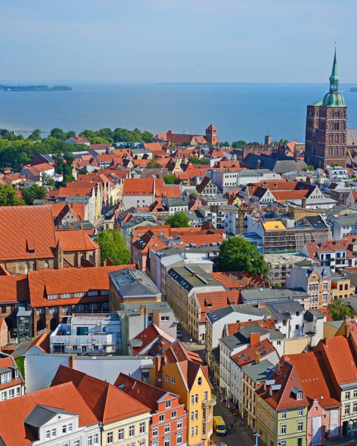 Stralsund aus der Vogelperspektive mit Blick auf den Kirchturm ganz rechts im Bild. Im Hintergrund die Ostsee